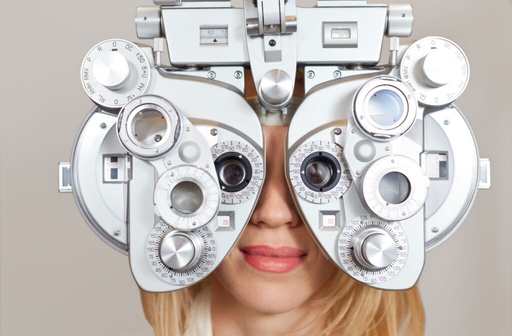A woman looking through a phoropter during an eye exam.