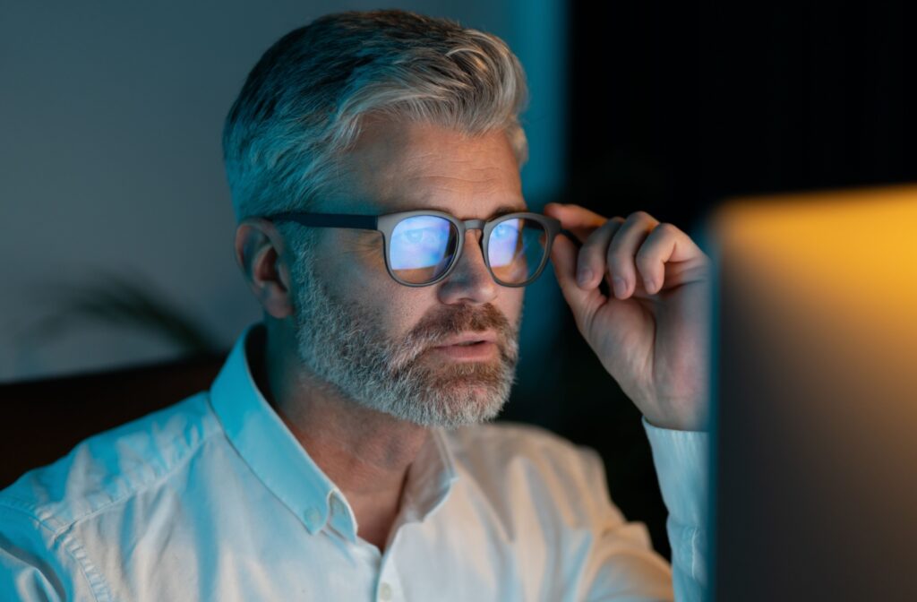 A person wearing blue light glasses to reduce blue light exposure is sitting in front of their computer in a dark room.