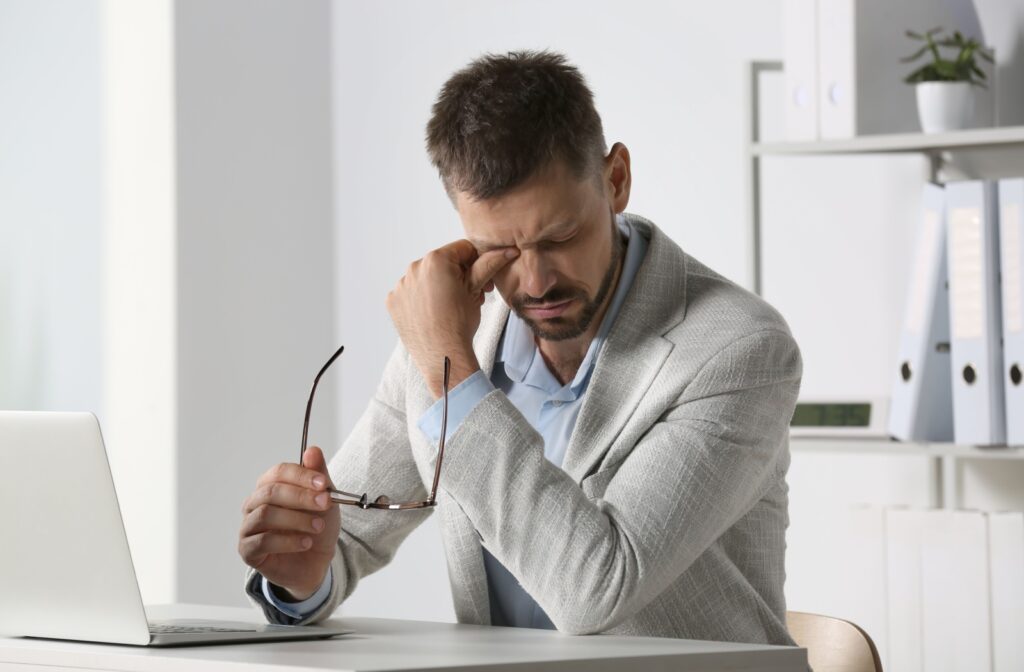 A person rubbing their eye while holding glasses, showing signs of eye strain.