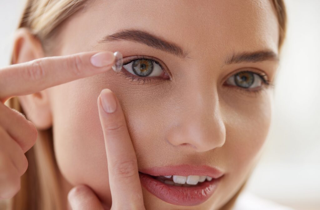 Close-up of a woman applying a soft contact lens to her right eye.