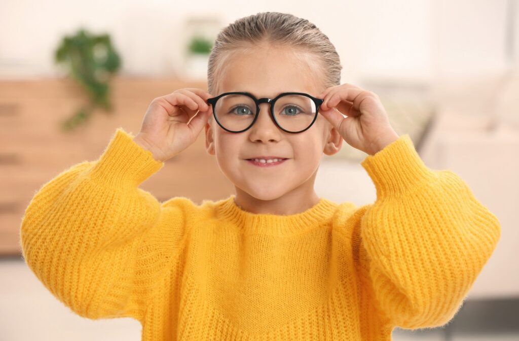 A child wearinig a yellow sweater holds the arms of the glasses that rest on their face