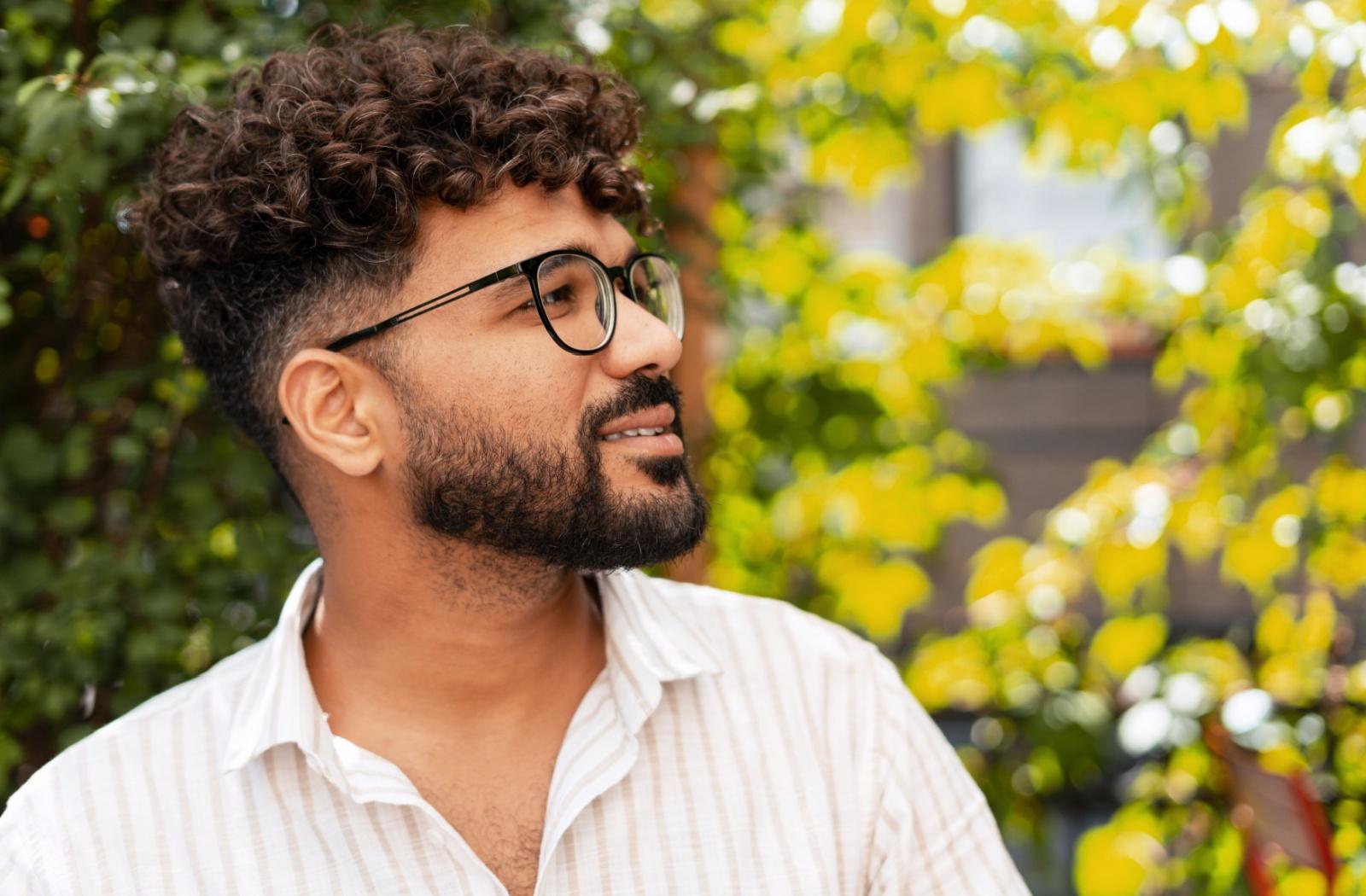 A person wearing black framed glasses outside and looking to the side